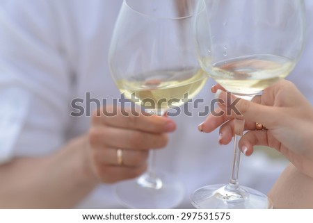 Man with ring in white and woman clinking glasses with white wine in toast for wedding holding goblets in hands sunny day outdoor on blur background closeup, horizontal picture