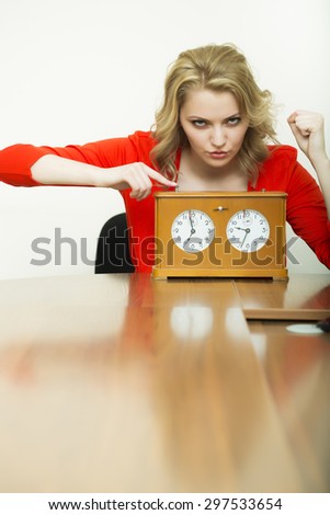 Pretty sexual waiting young blonde secretary girl sitting at table in red blouse with old wooden clock looking forward showing finger on time on white background copyspace, vertical picture