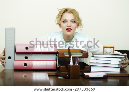 Beautiful young blonde business woman sitting in office at table with many documents files folders has a lot of work holding all items in heap on white background, horizontal picture