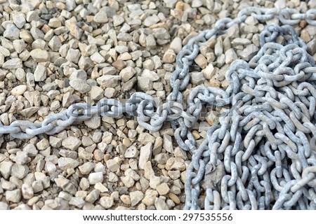 Natural background of many little coast pebble stones and long grey metal anchor chain cable with salt spots lying in heap in berth sunny day outdoor, horizontal picture