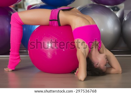 Pretty sexual straight fitness woman with musculat body lying in erotic pose on big pink ball in sport hall training indoor, horizontal picture