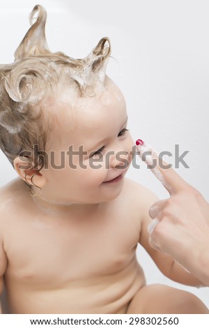 Small beautiful wet baby boy in bath room with foam soap hair sitting and playing with mother\'s hand on white background, vertical picture