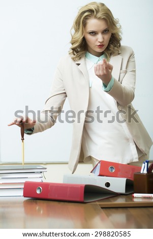 Pretty agressive blonde business woman in jacket standing near table with many folders holding knife for cutting paper asking to come looking forward on white background, vertical picture