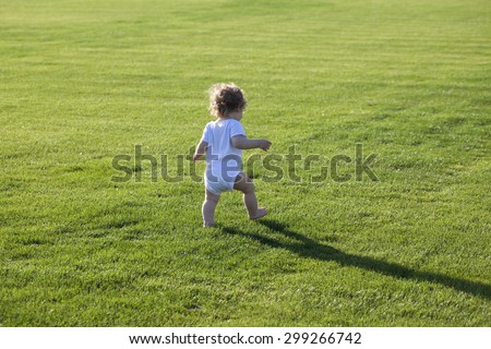 Happy runaway curly barefoot little boy on summer green grass meadow sunny day outdoor, horizontal photo