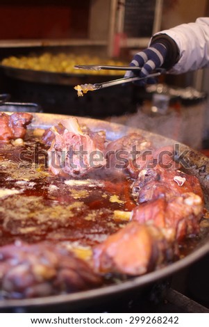 Cook fries delicious pieces of meat on bone in own juices in huge cauldron on fire outside, vertical photo