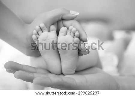 Happy family of mother and father touching bare feet with small toys and soft skin of little tiny child with male and female hands outdoor closeup black and white, hotizontal picture