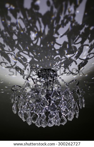 One beautiful glassy crystal hanging on high ceiling big chandelier making many flashes and shade of little sparkling lights on black and white background, vertical picture