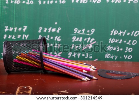 Colorful pencils of red yellow orange violet purple pink green and blue in stationary cup and ruler lying on brown school desk on written with white chalk blackboard backgroung on lesson of math