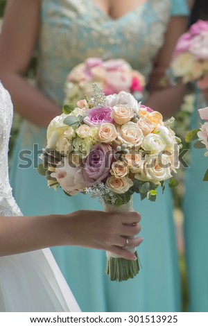 One beautiful fresh wedding bunch of colorful rose flowers pink violet lilac purple white orange and yellow in hands of bride and bridesmaid in blue dresses, vertical picutre