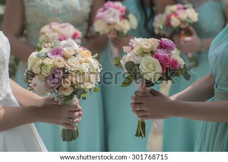Few beautiful fresh wedding posies of colorful rose flowers pink violet lilac purple white orange and yellow in hands of bride and bridesmaid in blue dresses, horizontal picutre
