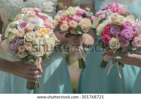 Three beautiful fresh wedding bouquets of colorful rose flowers pink violet lilac purple white orange and yellow in hands of bride and bridesmaid in blue dresses, horizontal picutre