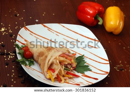 Pancake stuffed with sliced bacon sweet red green yellow pepper cheese and sauce with tomato and parsley on white plate on wooden table with vegetables coffee beans and gold stars, horizontal photo