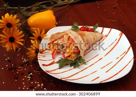Pancake stuffed with sliced bacon sweet red green yellow pepper cheese and sauce with tomato and parsley on white plate on wooden table with flowers coffee beans and gold stars, horizontal photo