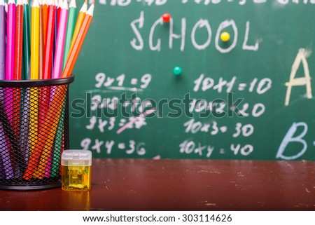 Colorful pencils of red yellow orange violet purple pink green and blue in stationary cup and steel standing on brown school desk on written with white chalk blackboard backgroung on lesson of math