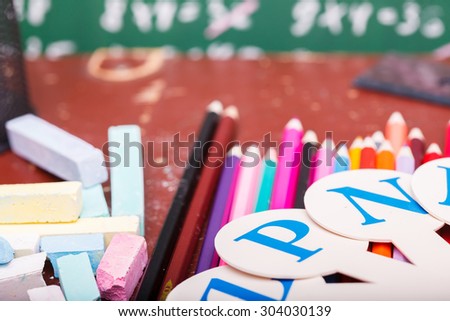 Colorful pencils of red yellow orange violet purple pink green blue ruler chalk and fan english alphabet with capital letters lying on brown school desk on written with white chalk blackboard