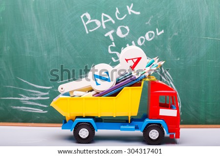 Colorful pencils of red yellow orange violet purple pink green blue chalk and fan english alphabet in plastic truck car toy lying on white school desk on back to school text, horizontal photo