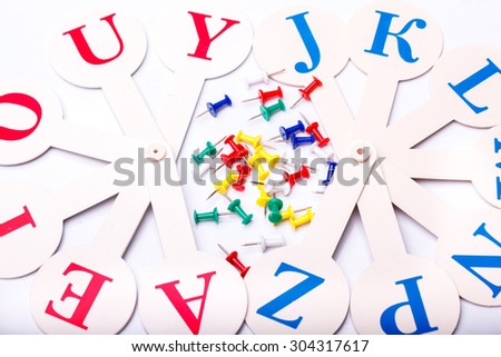 Many colorful drawing-pins of red yellow green blue colors and english alphabet fan with capital letters lying on white school desk background copyspace, horizontal photo