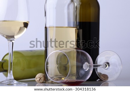 Composition of two glasses and bottles with white and red wine standing and lying with cork on table on white studio background, horizontal picture