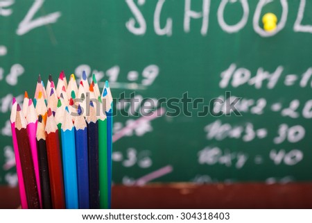 Colorful pencils of red yellow orange violet purple pink green and blue in stationary cup standing on school desk on written with white chalk blackboard background, horizontal picture