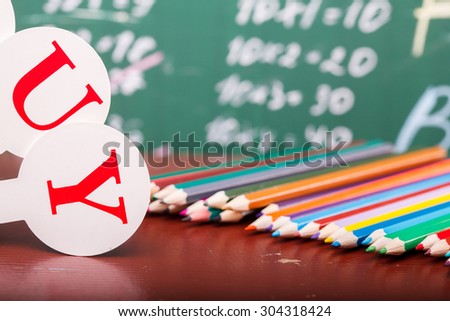 Colorful pencils of red yellow orange violet purple pink green and blue near fan english alphabet on brown school desk on written with white chalk blackboard on math