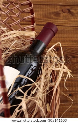 One glass wine corked new bottle full of alcohol red beverage wrapped in straw lying in wattled basket on wooden background closeup, vertical picture