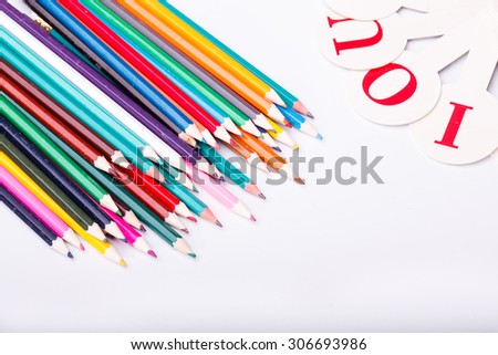 Colorful pencils of red yellow orange violet purple pink green blue chalk and fan english alphabet with capital letters lying on white school desk background copyspace, horizontal photo