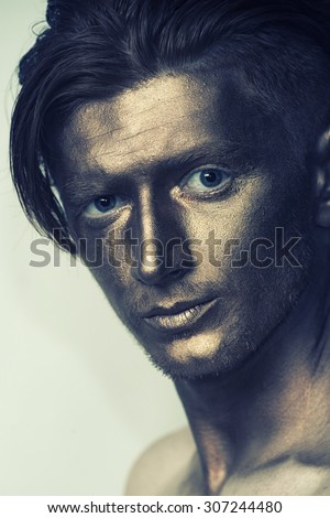Portrait of young fashionable painted boy model with bronze bodyart on face and stylish hairdo looking forward standing in studio, vertical picture