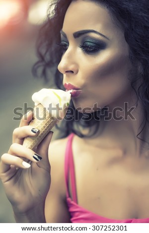 Closeup profile of sexy brunette attractive young lady with bright makeup eating cold dessert of red berry ice cream cone with mouth, vertical picture