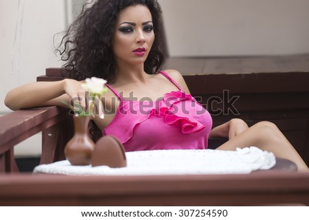 Young cute sexy brunette lady with curly hair sitting in cafe at table with vase of fresh white rose flower waiting looking forward, horizontal picture