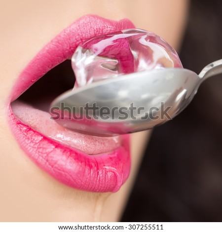 Closeup of pretty open female mouth of beautiful young woman with bright pink lips licking cold fresh crystal ice cube on silver colour spoon with tongue, square picture