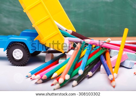 Colorful pencils of red yellow orange violet purple pink green blue chalk and fan english alphabet in plastic truck car toy lying on white school desk on blackboard background, horizontal photo