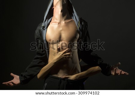 Young pair of man with sexual strong muscular body in leather jacket with hood looking up and woman embracing with hands standing on studio black background, horizontal picture