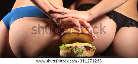 Two female bottoms of young girls in blue and black lace panties holding one big fresh tasty burger of green lettuce meat cutlet cheese onion and white bread bun with sesame seeds, horizontal picture