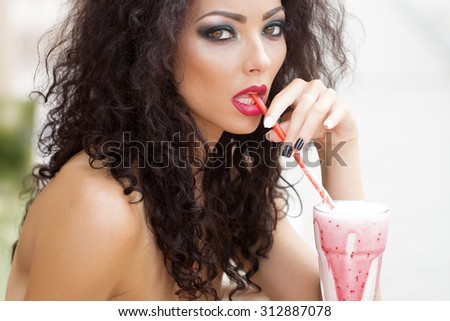 Awesome sensual magnificent young woman with bright makeup long brown curly hair with bare shoulders looking straight drinking cocktail through straw closeup on light background, horizontal picture