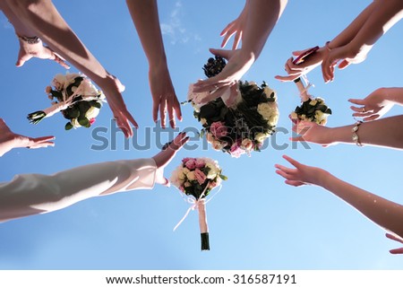 Women\'s hands trying catch four beautiful brides bouquets of roses pastel colors on clear blue sky background, horizontal photo
