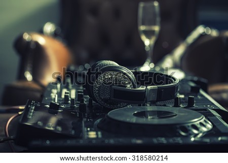 Dj musical mixer professional black console with many buttons and knobs and glamour headphones with pastes in night club or studio on brown leather sofa and wine glass background, horizontal picture