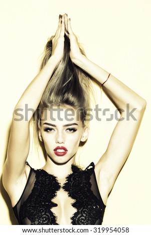 Fashionable emotional beautiful female model posing with long hair and red lips in stylish black clothes from lace standing with raised hands on studio background, vertical picture