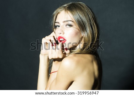 Portrait of one beautiful young sexual naked woman with long eyelashes lush hair and red lips holding hands near face looking forward standing in studio on black background, horizontal picture