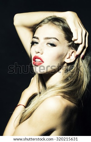 Portrait of beautiful sexual bare woman with long eyelashes lush hair and red lips holding raised hands near face and head looking forward in studio on black background, vertical picture