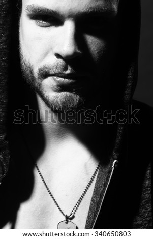 Closeup portrait of one serious handsome young sexual muscular man in open jacket with hood looking forward standing in studio black and white, vertical picture