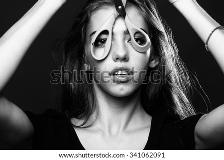 Closeup portrait of one beautiful young stylish woman holding scissors near face as professional hairdresser in studio black and white, horizontal picture