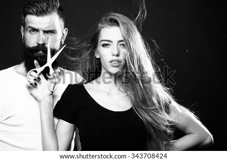 Closeup view of young beautiful couple of beautiful fashionable female barber cutting and holding scissors and handsome man with long beard in studio black and white, horizontal picture