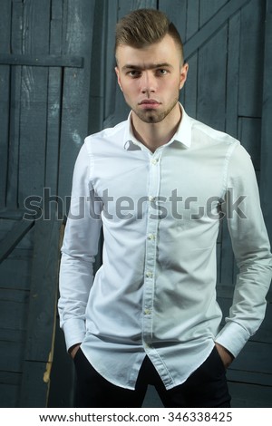 One sensual young handsome man with beautiful hairstyle in white shirt with bow standing in studio on wooden background, vertical picture