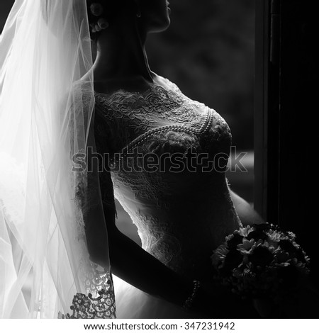 Photo closeup of beautiful young bride in ornamental wedding lace dress long veil holding elegant bouquet of fresh flowers for bridal ceremony black and white on grey background, square picture