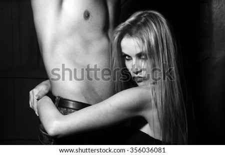 Young sexual couple of attractive blonde woman in bra embracing and sitting near handsome man naked muscular chest and torso in studio on wooden background, square picture