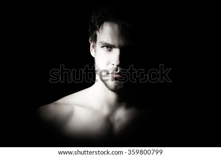 Closeup view portrait of one handsome bearded young macho man with strong look hazel eyes and sexy lips standing in light looking forward in studio on black background, horizontal picture