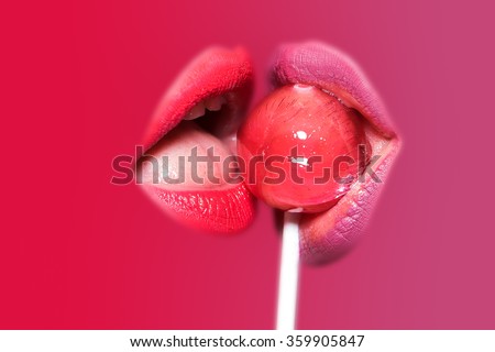 Closeup view of two sexy sensual bright female lips with juicy color lipgloss holding in mouth and licking delicious round red lollipop candy on stick isolated on pink purple background, horizontal