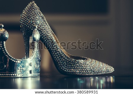 Female sprakling glamour luxury shoe on high heel and silver crown on reflecting table top close, glamour fashion concept, horizontal picture