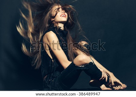 Attractive sensual young fashionable woman in stylish cloth and torn jeans with long beautiful hair sitting indoor on studio background, horizontal picture