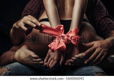 man holding female sexy buttocks of young woman with slim body and legs with bare back in lingerie has red ribbon bow on hands